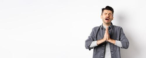 Miserable man begging for help, need something and crying, pleading with sad face, standing on white background desperate photo