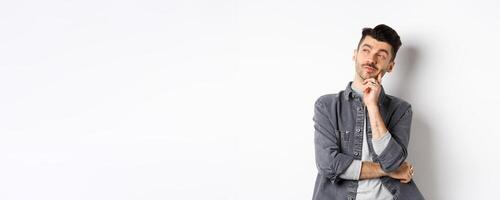 Thoughtful handsome man looking aside pensive, making choice, standing on white background photo