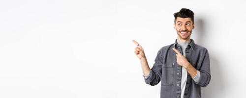 Happy handsome man smiling and pointing left at banner, showing cool product, standing on white background photo