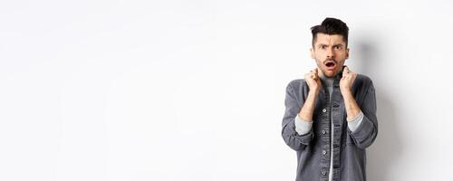 Shocked young man look confused and offended, gasping and frowning at camera, hear bad news, standing on white background photo