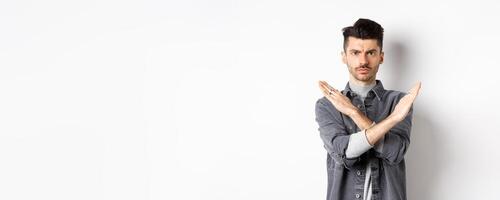 Angry man show cross gesture to stop or say no, frowning and looking serious, disagree and prohibit bad situation, standing on white background photo