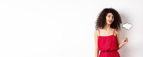 Beautiful woman with curly hair, wearing red dress, holding comment cloud, say something, standing on white background photo