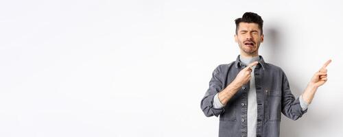 Crying man whining and complaining, pointing fingers right at sad news, standing miserable on white background photo