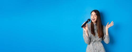 Beautiful candid girl singing in microphone, close eyes and smile carefree, sing at karaoke. Leisure and hobbies concept photo