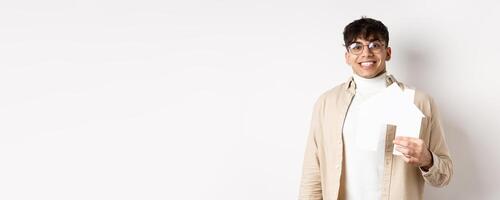 Real estate and mortgage concept. Cheerful young guy renting apartment, showing paper house cutout and smiling happy, buying property, white background photo