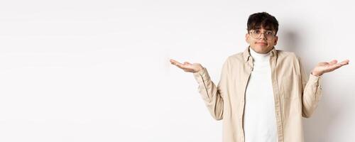 Portrait of handsome young man looking confused, know nothing, shrugging shoulders and spread hands sideways clueless, standing on white background photo