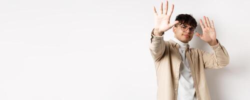 Image of reluctant and annoyed man raising hands up to block offer, refusing and asking to stop, telling no, declining something, standing on white background photo