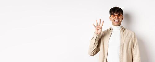 Handsome young man making order, showing number four fingers and smiling, standing on white background photo