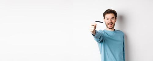 Happy man showing plastic credit card and smiling, recommending bank, standing over white background photo