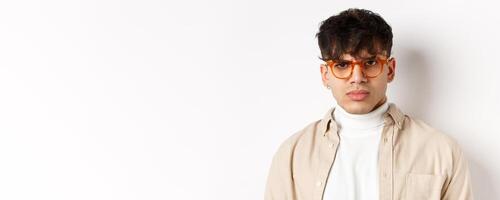 Close up portrait of angry frowning guy looking with despise, standing mad on white background, wearing glasses photo