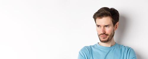 Close-up of disappointed bearded man, sulking and looking left with pensive face, standing upset over white background photo
