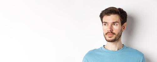 Close-up of handsome male model with beard and moustache, looking left with thoughtful face, standing over white background photo