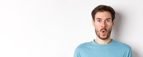 Close-up of surprised man face, saying wow and staring at camera amazed, standing on white background photo