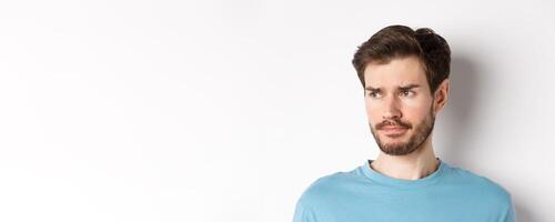 Close-up of disappointed sad man, grimacing and frowning, looking left upset, standing doubtful against white background photo
