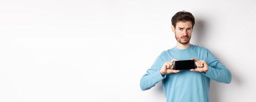 E-commerce and shopping concept. Sad and disappointed guy complaining, showing empty smartphone screen, standing on white background photo