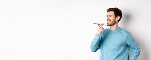 Young man talking on speakerphone or translating voice recording on application, standing happy on white background photo