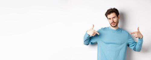 Young man with beard feeling confident, pointing at himself and making smug face, standing on white background cool and sassy photo