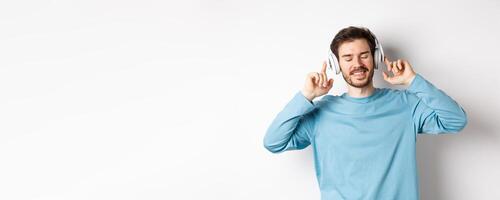 Handsome man listening music in wireless headphones and smiling, enjoying good sound, white background photo