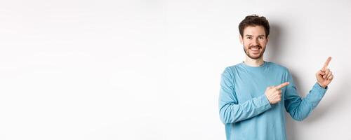 Happy bearded man showing advertisement, pointing fingers right and smiling, inviting to click link, standing over white background photo