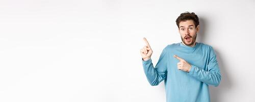 Amazed man showing awesome promo offer, pointing fingers at upper left corner logo and looking excited, recommend product, white background photo
