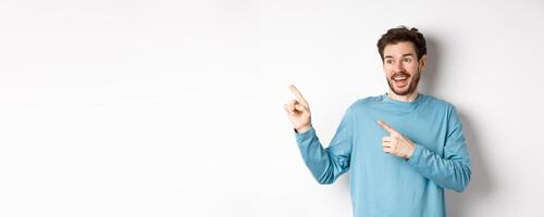 Excited bearded man checking out special offer, pointing and looking at advertisement with happy face, standing over white background photo