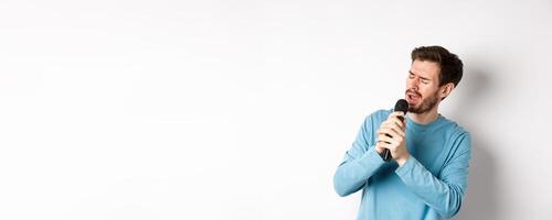 Romantic man singing song in microphone at karaoke, standing over white background photo