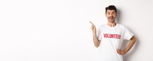 Happy smiling volunteer pointing finger left at copy space, showing announcement, white background photo