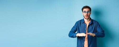 Funny guy trying sunglasses at eyewear store, dancing and having fun, standing on blue background photo