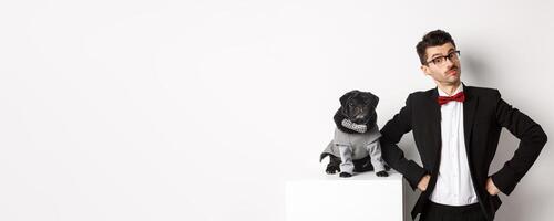 Animals, party and celebration concept. Handsome young man and puppy in formal suits looking at camera, standing over white background photo
