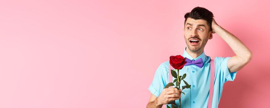 nervioso hombre esperando para su fecha en san valentin día, participación rojo Rosa y mirando confuso oblicuo, rascarse cabeza ansiosamente, en pie en rosado antecedentes foto