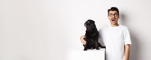 Image of amazed man staring at camera while his small dog looking left at copy space, standing over white background photo