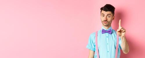 Young funny guy showing finger to explain something, prohibit or warn you, standing on pink background photo