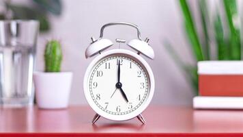 Classic white clock on a table. The clock hand points to 5 or 17, close up photo