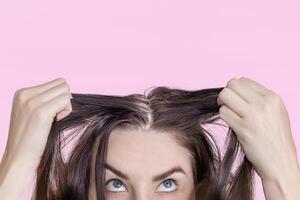 Caucasian brunette woman shows grown gray hair. Isolated on pink background. Close up photo