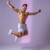 A Shirtless Man Jumps With Arms Spread Against Purple Background photo