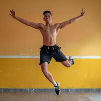 Young Man Jumping With Arms Outstretched in Front of a Yellow Wall photo