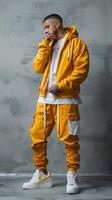 Man Wearing Yellow Hoodie and Pants Posing In Front Of Grey Wall photo
