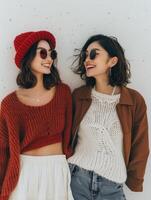 Two Women Wearing Knit Sweaters and Sunglasses Smile at Each Other photo