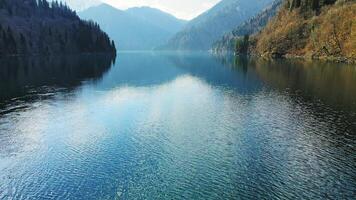 Clear blue mountain lake with reflection of clouds on the water. Drone view video