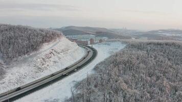 Flight of the drone from the road with traffic among the mountains in winter. video