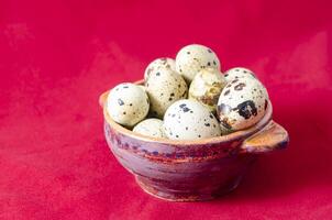 Quail eggs in clay bowl, red background photo
