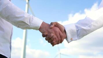 Close up two multiracial man wind turbine engineers working and shaking hands at wind turbine farm on background, renewable energy video