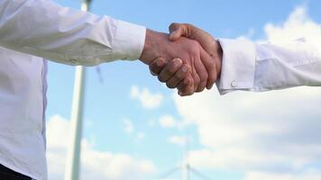 Close up two multiracial man wind turbine engineers working and shaking hands at wind turbine farm on background, renewable energy video