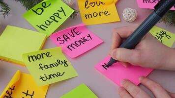 Unrecognizable woman writing new year's resolutions on colorful sticky notes. Making promises for new year, setting goals. Creating vision board motivation video