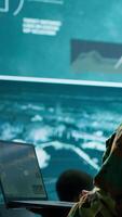 Vertical Military officer oversees surveillance and cybersecurity operations in a high tech army command post, ensuring the protection of classified information and data integrity. Big screen gear. Camera A. video