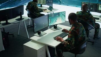 Military experts in mission control center use modern technology on computer and big screen, analyzing satellite footage. Specialist tracking potential threats for intelligence operations. Camera B. video