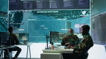 High tech military office with soldiers analyzing real time data, processing intelligence information and coordinating strategic operations to support army field missions effectively. Camera B. video