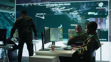 Team of military specialists in command post monitoring satellite data, integrates real time information from cctv footage. Decision making for strategic defense missions and security. Camera B. video