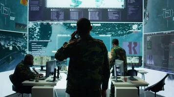 Military man answers phone call in a mission control center, working with advanced technology and satellite imagery to track potential threats and real time data. Intelligence activities. Camera B. video