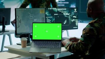 IT expert collecting real time information next to isolated chroma key screen, high tech gear in command post. Soldier processing intelligence for field operations and strategic missions. Camera A. video